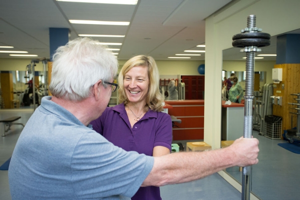 Eine Therapeutin zeigt dem Rehabilitand eine Übung mit einer Hantel Eine Therapeutin zeigt dem Rehabilitand eine Übung mit einer Hantel